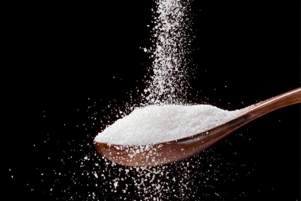 מזיגת אריתריטול לכף עץ על רקע שחור - תחליף סוכר קטוגני